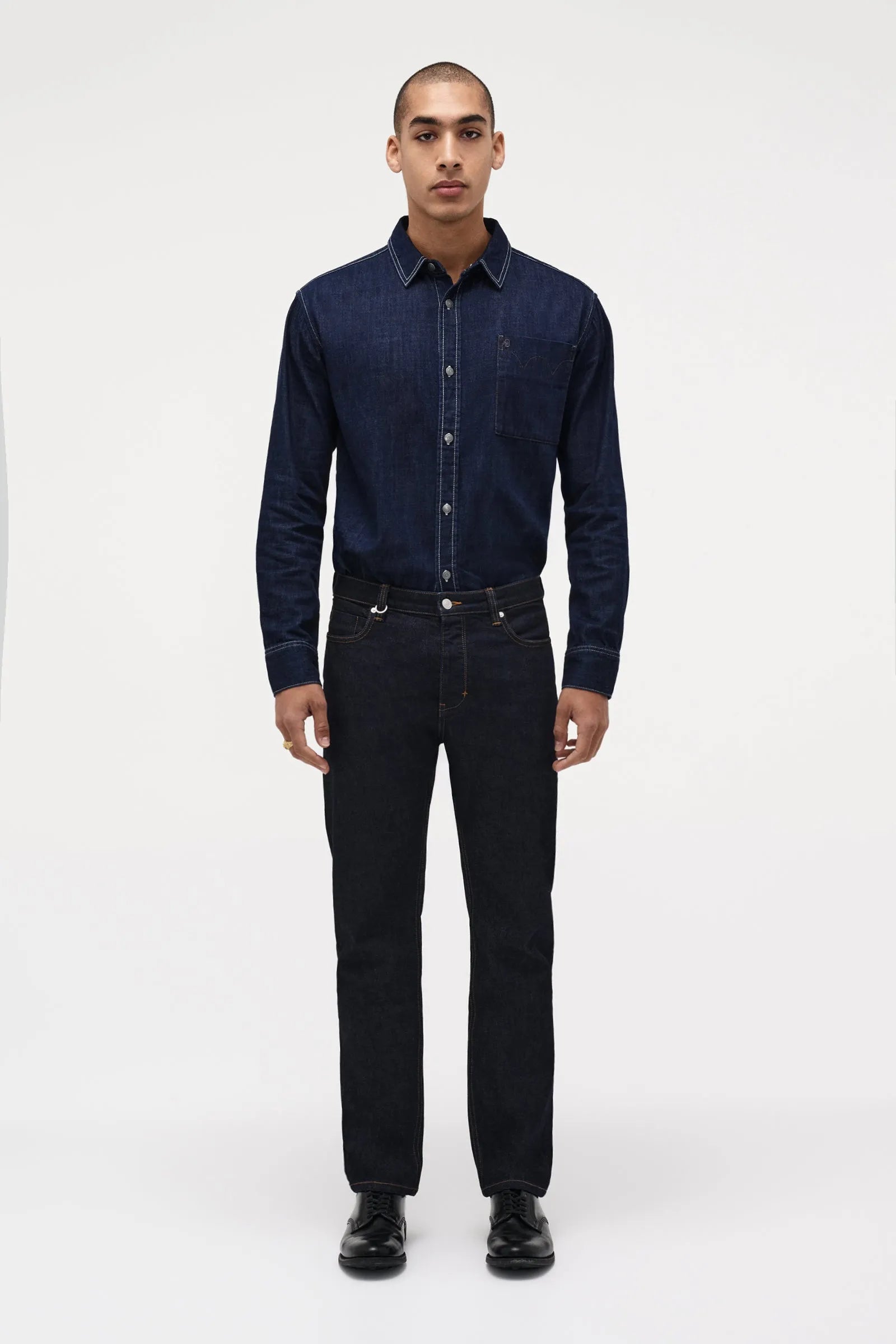 Man wearing a dark denim shirt and jeans on a white background