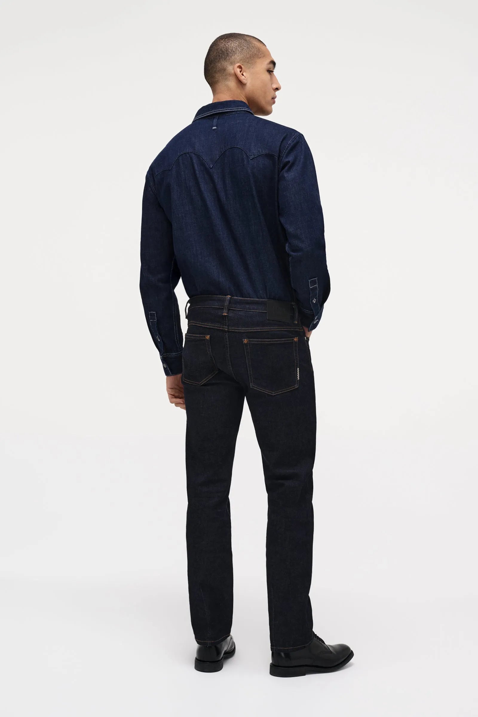 Man wearing a dark blue shirt and black jeans on a white background